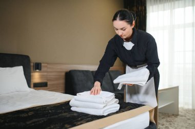 Oda hizmetçisi havlu katlarken otel odasında yatak yapıyor..