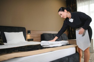 Hizmetçi otel odasında çiçekli temiz havlular tutuyor..
