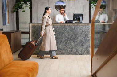 Female guests come with bags and suitcases to the hotel reception in the lobby.