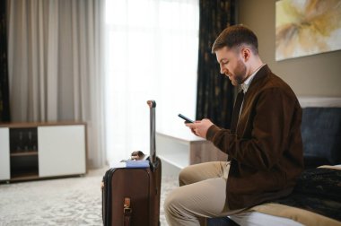 Neşeli iş adamı iş gezisinde otel odasında telefon kullanıyor..