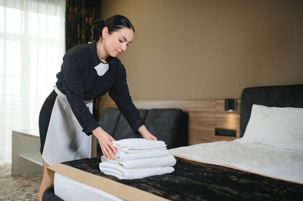Maid holding fresh towels with flowers in hotel room.