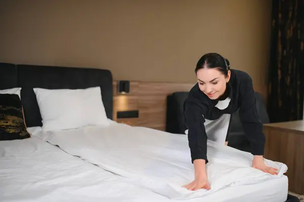 Young hotel maid making the bed.