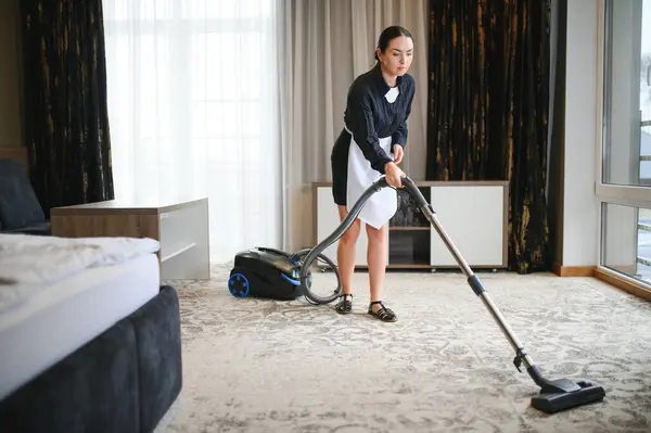 Hotel service. female housekeeping worker with vacuum cleaner in room apartment.