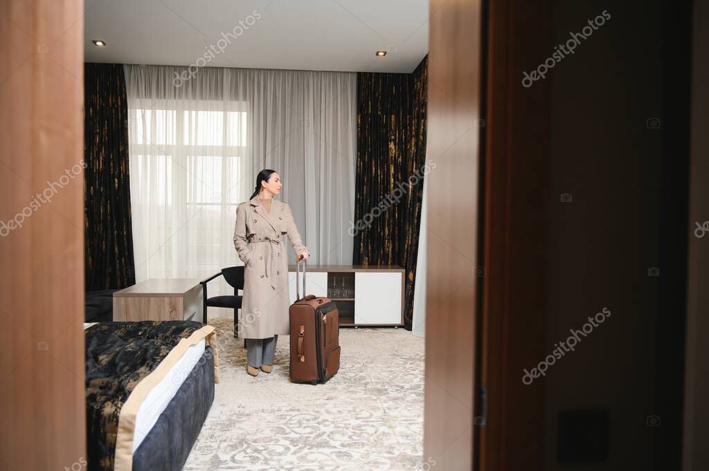 Business woman walking into hotel room with luggage.
