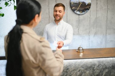 Otel lobisinde beyaz gömlek giyen genç bir resepsiyonistin portresi..