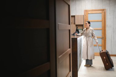 Lüks otelin lobisinde bavullu şık bir iş kadını. İş seyahati ve evcil hayvan dostu otel konsepti.