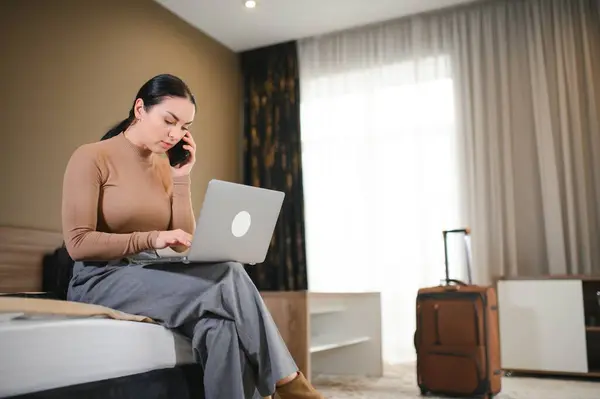 businesswoman with laptop computer sitting in hotel on bed and working late in hotel room, with her laptop computer.