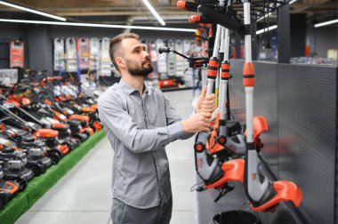 Bahçe gereçleri dükkanında elinde elektrikli çim biçme makinesi olan mutlu bir müşteri..