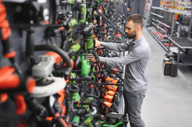 Hırdavatçıdaki bir adam yeni bir tornavida seçiyor. Yanında da tamirat için kullanılan elektrikli aletler var.