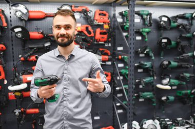 Genç bir adam hırdavatçıda güçlü bir matkap seçer..