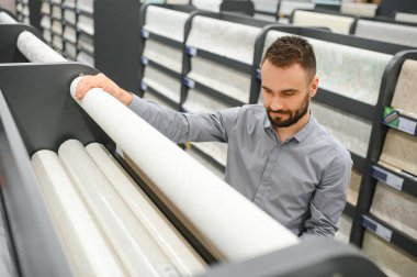 Bir adam hırdavatçıdaki duvarları yapıştırmak için duvar kağıdı seçer..