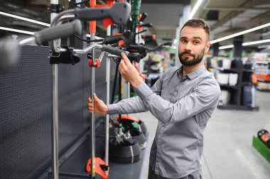 Bahçe gereçleri dükkanında elinde elektrikli çim biçme makinesi olan mutlu bir müşteri..