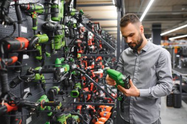 Hırdavatçıdaki bir adam yeni bir tornavida seçiyor. Yanında da tamirat için kullanılan elektrikli aletler var.
