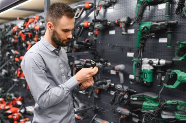 Genç bir adam hırdavatçıda güçlü bir matkap seçer..