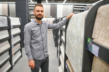 Bir adam hırdavatçıdaki duvarları yapıştırmak için duvar kağıdı seçer..