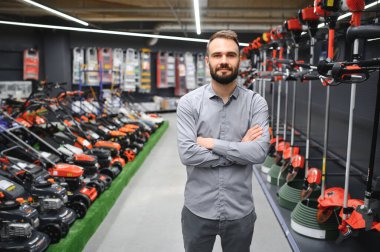 Bahçe gereçleri dükkanında elinde elektrikli çim biçme makinesi olan mutlu bir müşteri..