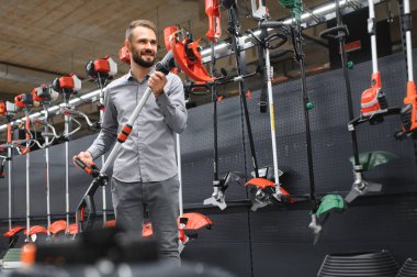 Bahçe gereçleri dükkanında elinde elektrikli çim biçme makinesi olan mutlu bir müşteri..