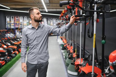 Bahçe gereçleri dükkanında elinde elektrikli çim biçme makinesi olan mutlu bir müşteri..