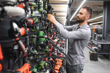 Genç bir adam hırdavatçıda güçlü bir matkap seçer..