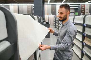 Bir adam hırdavatçıdaki duvarları yapıştırmak için duvar kağıdı seçer..