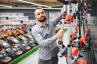 Bahçe malzemeleri dükkanındaki genç bir adam çim biçmek için elektrikli budama makinesi seçiyor..