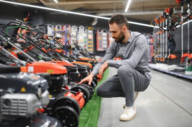 Müşteri, bahçıvanlar ve bahçıvanlar için elektrikçi dükkanındaki yeni çim biçme makinesi modellerini inceler..