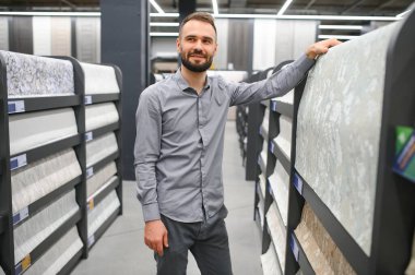 Bir adam hırdavatçıdaki duvarları yapıştırmak için duvar kağıdı seçer..
