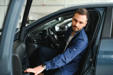 Genç adam yeni bir araç içinde araba Bayilik seçmektir.