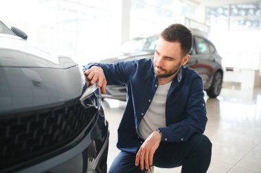 Genç adam yeni bir araç içinde araba Bayilik seçmektir.