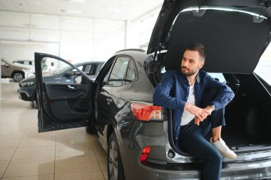 Genç adam yeni bir araç içinde araba Bayilik seçmektir.