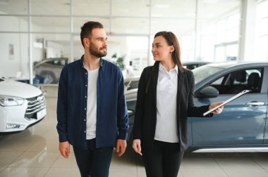 Dost canlısı, güler yüzlü bayan satıcı araba kuaföründe dururken müşteriye yepyeni bir araba gösteriyor..