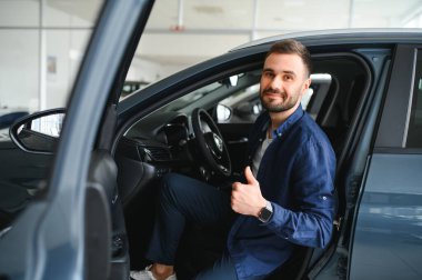 Genç adam yeni bir araç içinde araba Bayilik seçmektir.