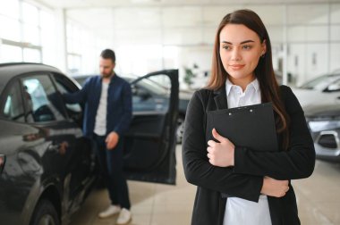 Gülümseyen satıcı kadın araba galerisinde belgeyi tutuyor..