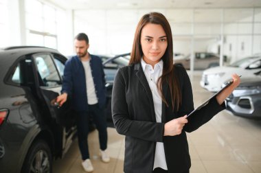 Gülümseyen satıcı kadın araba galerisinde belgeyi tutuyor..