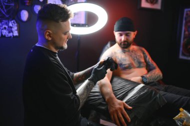 Stüdyoda çalışan sakallı dövme sanatçısı erkek müşterisinin koluna dövme yapıyor. Profesyonel dövmeci tarafından dövme yaptıran bir adam..