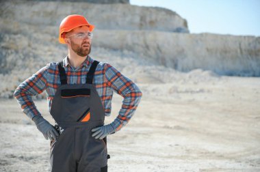 Portrait of a worker standing on the background of a stone quarry. clipart