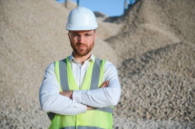 Kask takan bir işçi taş parçalayan bir fabrikada duruyor..