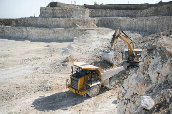 stock image Heavy mining truck and excavator, close-up, against the background of the panorama of a limestone quarry.