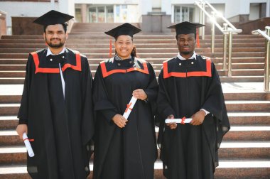 Eğitim, mezuniyet ve halk konsepti. Havan topu ve diplomalı bekarlık elbisesi giyen bir grup mutlu uluslararası öğrenci..