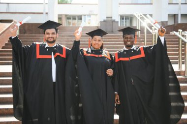 Eğitim, mezuniyet ve halk konsepti. Havan topu ve diplomalı bekarlık elbisesi giyen bir grup mutlu uluslararası öğrenci..