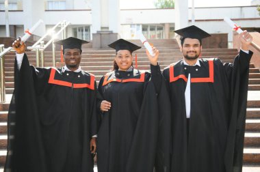 Eğitim, mezuniyet ve halk konsepti. Havan topu ve diplomalı bekarlık elbisesi giyen bir grup mutlu uluslararası öğrenci..