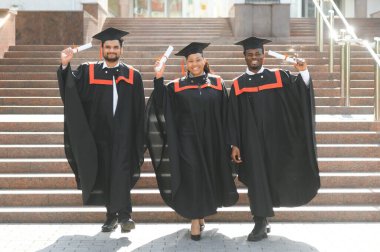 Eğitim, mezuniyet ve halk konsepti. Havan topu ve diplomalı bekarlık elbisesi giyen bir grup mutlu uluslararası öğrenci..