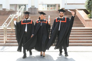 Eğitim, mezuniyet ve halk konsepti. Havan topu ve diplomalı bekarlık elbisesi giyen bir grup mutlu uluslararası öğrenci..