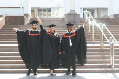 Eğitim, mezuniyet ve halk konsepti. Havan topu ve diplomalı bekarlık elbisesi giyen bir grup mutlu uluslararası öğrenci..