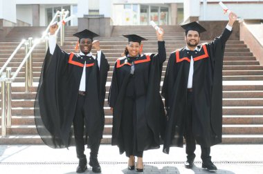 Eğitim, mezuniyet ve halk konsepti. Havan topu ve diplomalı bekarlık elbisesi giyen bir grup mutlu uluslararası öğrenci..