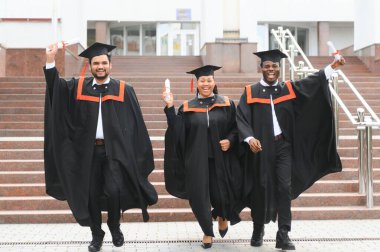 Eğitim, mezuniyet ve halk konsepti. Havan topu ve diplomalı bekarlık elbisesi giyen bir grup mutlu uluslararası öğrenci..