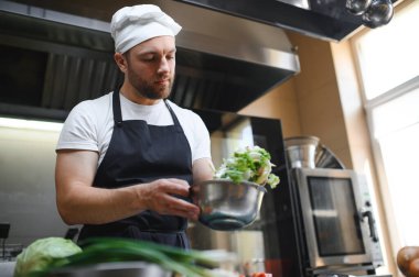 Üniformalı aşçı restoran mutfağındaki büyük ocakta yemek pişiriyor..