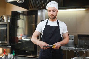 Üniformalı aşçı restoran mutfağındaki büyük ocakta yemek pişiriyor..