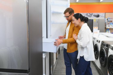 Genç çift, memnun müşteriler eşyalar mağazasında buzdolabı seçiyor..