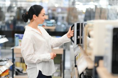 Genç bir kadın hipermarkette yeni bir mikrodalga fırın seçti..